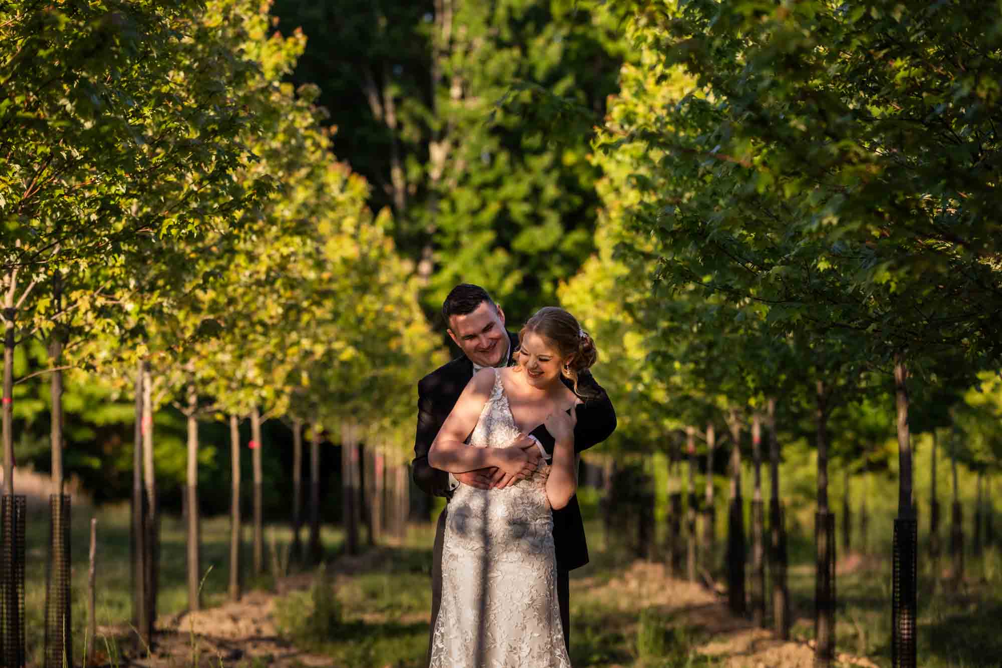 bride and groom posing in between rows of trees growing on the eisler farm wedding venue, pinehall